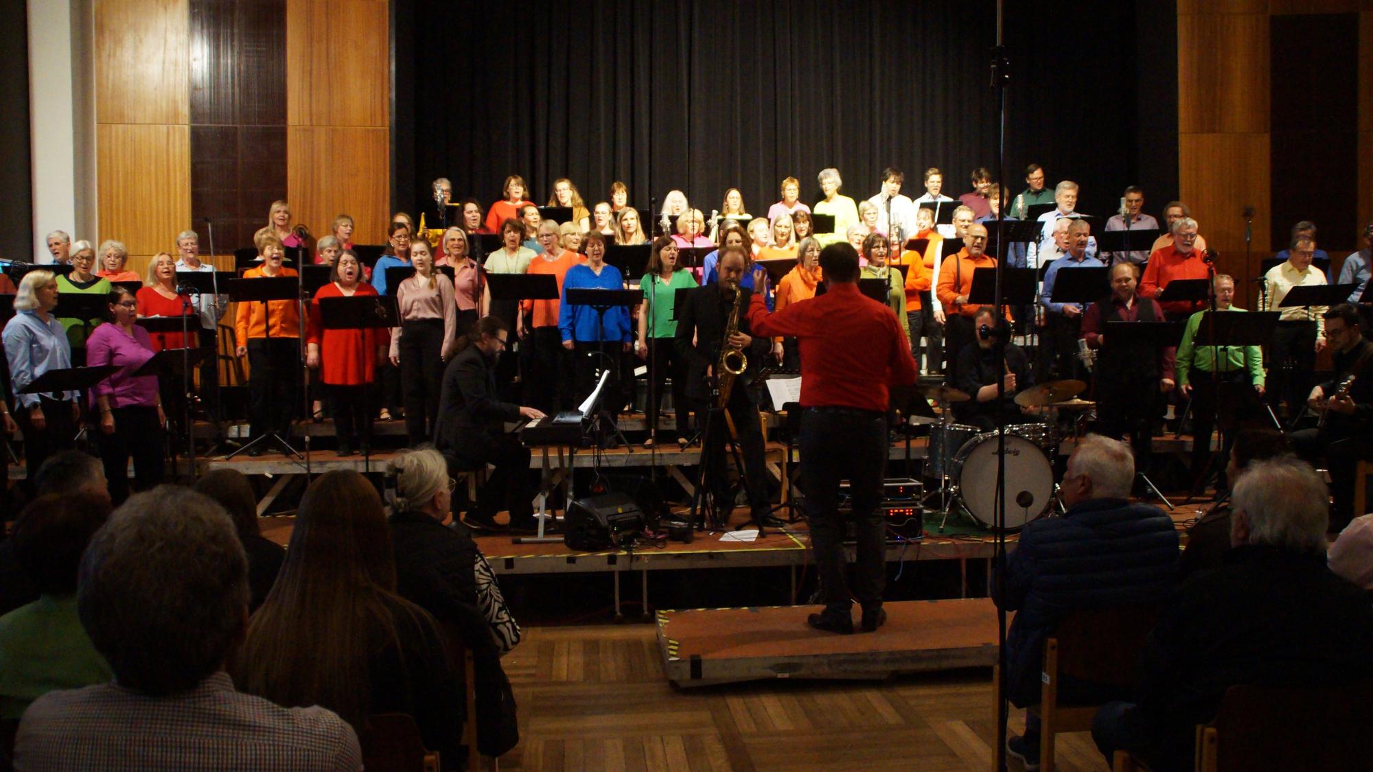 Der Bunt gekleidete Chor steht hinter der Jazz-Band auf der Bühne in der Stadthalle Schweinfurt.